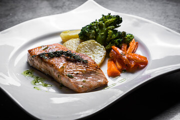 Plato de salmón a la plancha cocinado en restaurante y servido en plato blanco con forma cuadrada acompañado con verduras, patata y zanahoria 