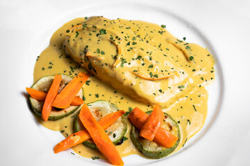 Pescado en salsa con verduras servido en plato blanco con zanahoria con salsa amarilla para clientes