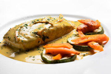 Pescado en salsa con verduras servido en plato blanco con zanahoria con salsa amarilla para clientes