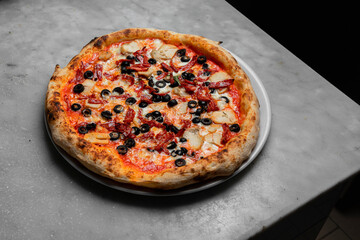 Pizza al estilo italiano con aceitunas negras, tomate queso en plato blanco redondo
