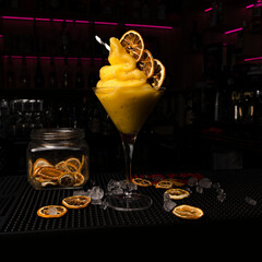 Bebida helada amarilla con alcohol con fruta deshidratada y mucho hielo en coctelería y el fondo...