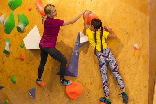Young female bouldering instructor helping boy climb artificial wall