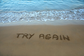 Try again written in the sand on the beach with the sea washing up the shore