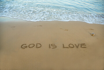 God is love written in the sand on the beach with the sea washing up the shore