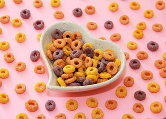 children's dry breakfast round multicolored rings in a decorative plate in the form of a heart on a pink background