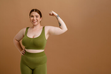 Young beautiful smiling happy plus size girl showing her bicep - obrazy, fototapety, plakaty