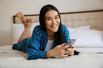 Asian girl using laptop and mobile phone while lying in bed at home