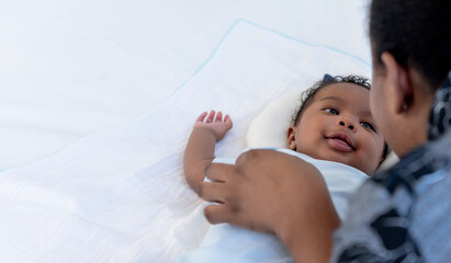 an African newborn baby is 2 months old lying on a white bed smiling happily When he is looking at...