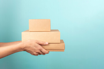 Stack of cardboard boxes in female hands. Blank brown parcel boxes on light blue background. Mock...
