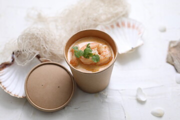 Thai tom kha soup with king prawns. Oriental shrimp soup in a take-away carton box, on a white...