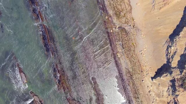 Straight down aerial view of the waves washing ashore at RCA Beach in central California along the sandstone cliffs