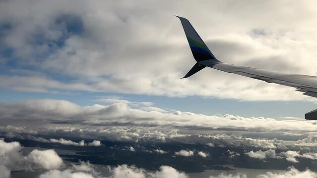 Airplane wing tip turning and descending above the clouds