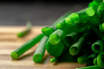 Stems of fresh green onions on striped wooden kitchen board. Macro shot of juicy cut stalks of green scallion. Cutaway green shallot or chive stalk. Greenery, seasoning for cooking fresh healthy salad - obrazy, fototapety, plakaty