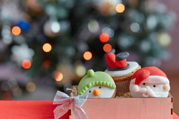 Aesthetic cozy Christmas cupcakes in wooden box. Gift in front of the bokeh of Christmas tree. Good holidays mood. Selective focus
