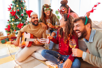 Friends playing the guitar, singing Christmas songs and drinking wine