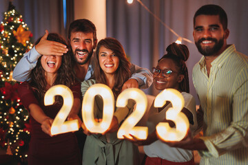 Friends holding illuminative numbers 2023 while celebrating New Year