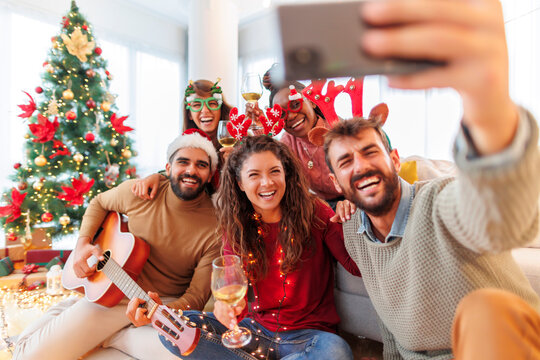 Friends taking selfies, playing the guitar and singing while celebrating Christmas