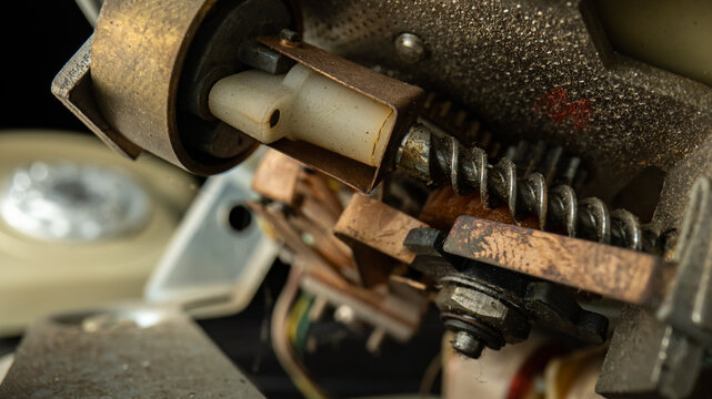Internal mechanism of an old disassembled rotary telephone. Threaded metal screws, nuts, gears, dusty plastic parts. A macro shot of the details of a broken vintage landline phone. Repair in workshop.
