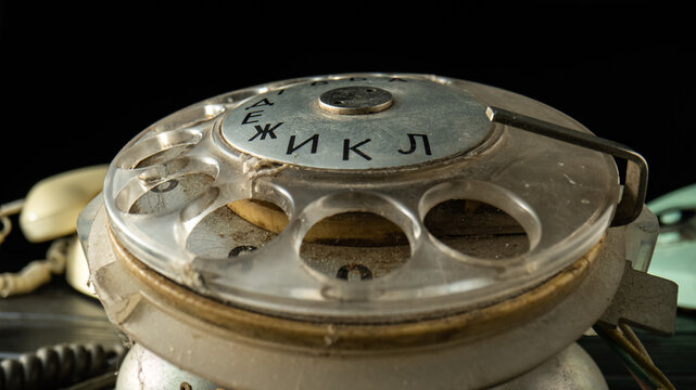 Rotary dialer of an old dirty telephone with round holes and numbers on a black background. Plastic transparent dialing disc in the dust on analog vintage landline phone. Macro shot.