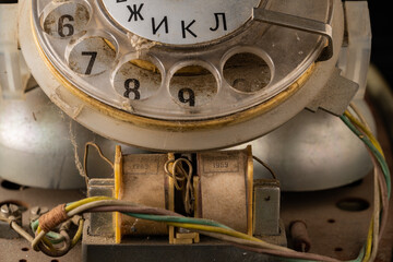 Old disassembled rotary telephone with internal parts green, yellow and white twisted wires in the dust. Macro shot of vintage broken rotary dialer with round holes and numbers. Retro landlines. - obrazy, fototapety, plakaty
