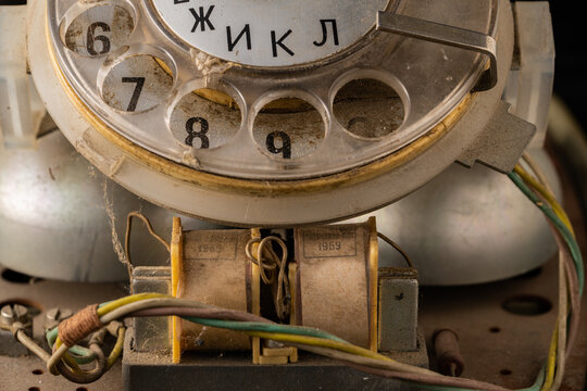 Old disassembled rotary telephone with internal parts green, yellow and white twisted wires in the dust. Macro shot of vintage broken rotary dialer with round holes and numbers. Retro landlines.