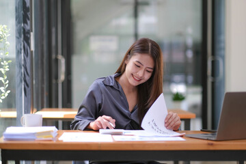 Asian Businesswoman using a calculator and laptop computer for doing math finance on a wooden desk, tax, accounting, statistics report and analytical research concept.