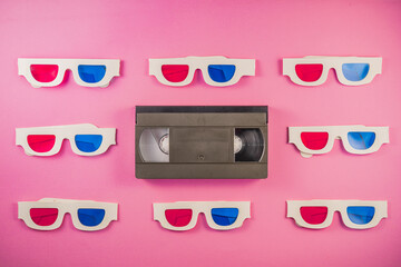 Old white paper 3d glasses with blue red lenses and black videotape on pink background. Retro video...