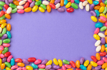 Frame of colorful candies over purple background with copy space