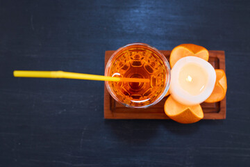 Orange and a glass of juice with yellow pipe on wooden platter
