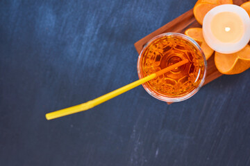 Orange and a glass of juice with yellow pipe on wooden platter on the top corner