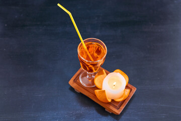 Orange and a glass of juice with yellow pipe on wooden platter, angle view
