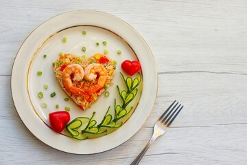 Heart shaped shrimps fried rice served with heart shaped cucumbers and tomatoes on plate with white wood background.Creative art food idea for Valentine and Mother day.Top view.Copy space