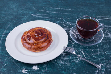 A cup of espresso with pastry bun in a white plate on blue background