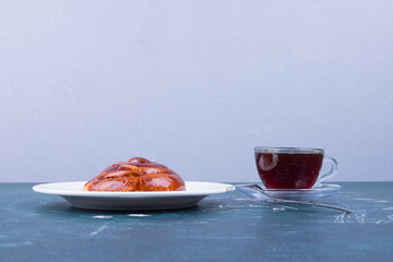 A cup of espresso with pastry bun in a white plate isolated on blue