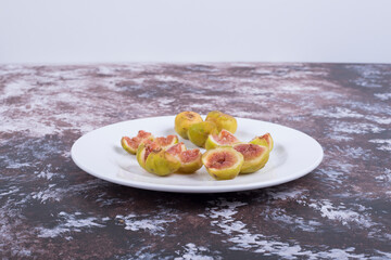 Yellow figs with red seeds in a white plate isolated on blue background