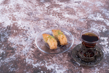 A glass of tea with turkish pakhlava in glass saucer on marble table