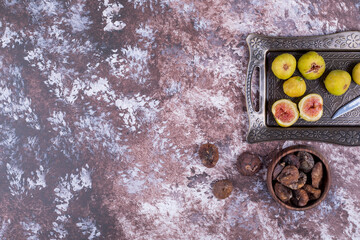 Whole, dry and sliced figs in a metallic tray and in a wooden cup, top view