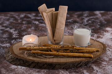 Snacks and crackers with a glass of milk on rustic background with a flaming candle