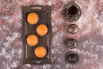 A glass of tea in ethnic dishes served with cupcakes