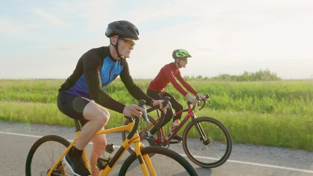 Group of cyclists in helmet riding sport bikes during sunset time. Two fit athletes in sunglasses training intensive before international competition.