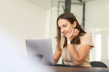 Portrait of a young caucasian woman sitting at the desk with a laptop, typing an email, messaging friend, chatting, dating online with a pleasant smile, long-distance relationships concept