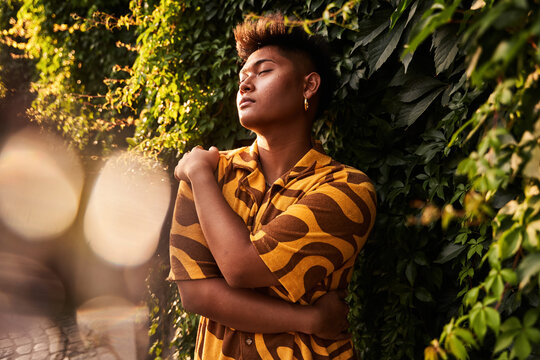 Sensual non binary guy embracing himself in garden