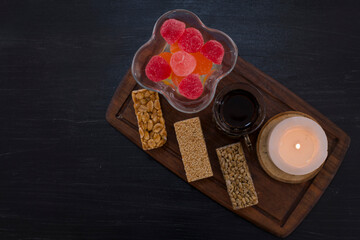 A glass of tea served with marmelades and sesame waffles with a candle aside on a wooden platter