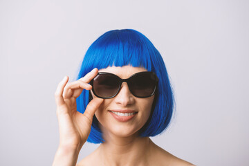 Beauty, fashion concept. Portrait of beautiful and sexy woman with blue wig and sunglasses looking to camera with smile. Model with naked shoulders. Toned image with soft yellow color