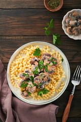 Fusilli pasta with mushrooms, cheese and garlic creamy sauce on plate on old wooden dark table background. Top view. Traditional Italian cuisine.