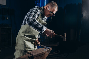 Senior an artisan blacksmith knocks with a hammer on iron to shape