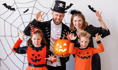 Cheerful family   in carnival costumes celebrate Halloween and does scary gesture near gray wall with cobwebs and bats - obrazy, fototapety, plakaty