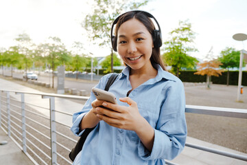 Asian brunette woman using cellphone while standing on city street