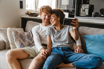 Young multinational couple taking selfie photo on cellphone at home