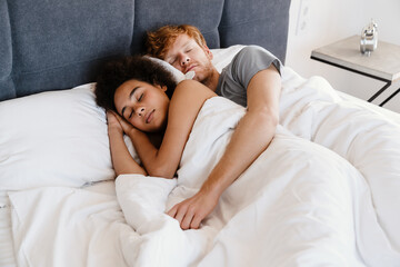 Young multinational couple hugging and sleeping together at home